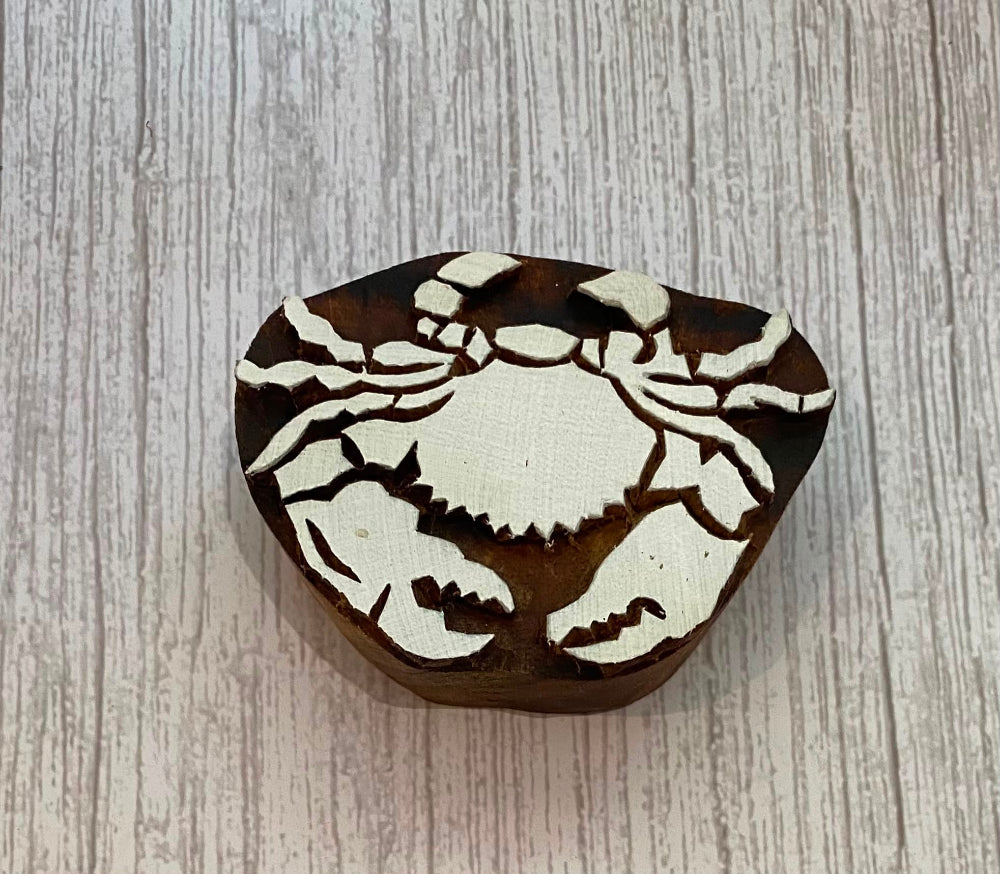 A carved wooden crab-shaped box or container with a dark brown finish and a contrasting light beige inlay, shown on a light gray wood-textured background.